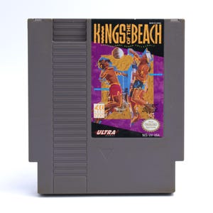 May include: A gray Nintendo Entertainment System (NES) cartridge for the game "Kings of the Beach." The label features two volleyball players in action, with a purple and yellow background. The cartridge is labeled "Ultra Games."