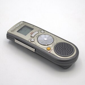 May include: A silver Olympus Digital Voice Recorder with a black speaker and buttons labeled "REC", "STOP", "PLAY", and "ERASE".