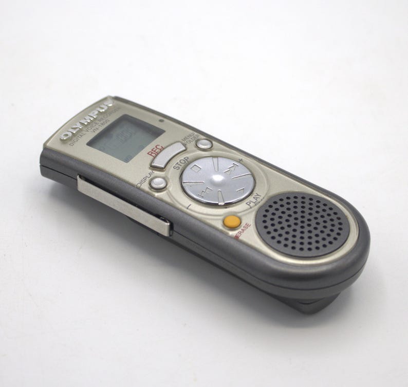 May include: A silver Olympus Digital Voice Recorder with a black speaker and buttons labeled "REC", "STOP", "PLAY", and "ERASE".