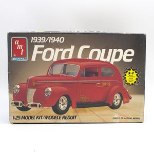 May include: A vintage model kit box for a 1939/1940 Ford Coupe. The box features a red car illustration with chrome wheels and the text "Ford Coupe". The box also includes the text "1:25 Model Kit".