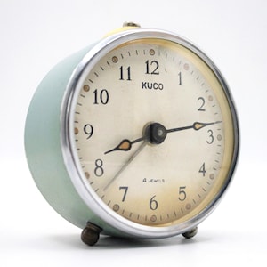 May include: A vintage green alarm clock with a white face and black hands. The clock has a chrome bezel and says "KUCO" and "4 JEWELS" on the face.