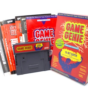 May include: A red and yellow Game Genie cartridge for the Super Nintendo Entertainment System. The cartridge is in its original packaging, which features a muscular cartoon character and the text "16-Bit Super". The packaging also includes a stack of instruction manuals.