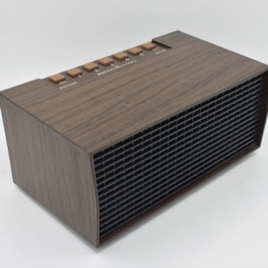 May include: A brown woodgrain electric heater with a black metal grill and a row of buttons on the top. The buttons are labeled "OFF", "INSTANT", "FAN", "1", "2", "3", and "4".