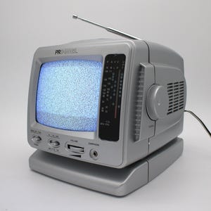 May include: A silver portable television with an antenna and a built-in radio dial. The screen displays static. The TV has a volume knob, tuning dial, and an earphone jack. The brand name "PRO IMAGE" is visible on the top.