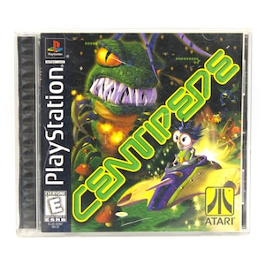 May include: A PlayStation game case for Centipede 3D. The cover art features a green monster with large teeth, a character in a vehicle, and the game title in green. The Atari logo is visible.