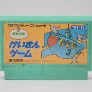 May include: A vintage mint green video game cartridge. The label features Japanese text and a cartoon submarine with the number 3. The game title is "Keisan Game". The cartridge is labeled "TKS-S3" and was published by Tokyo Shoseki Co. Ltd.