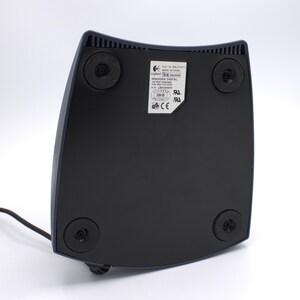 Puede incluir: Base de mando de juegos Logitech WingMan Digital negra y azul marino, vista desde abajo. La base tiene cuatro patas de goma negras y una etiqueta con informaci&oacute;n del producto. Un cable negro se extiende desde la base.