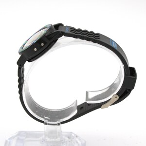 May include: Black sports watch with a textured black band and a multi-colored face. The watch has a digital display and a buckle closure. The band has the word "SPORT" printed on it.