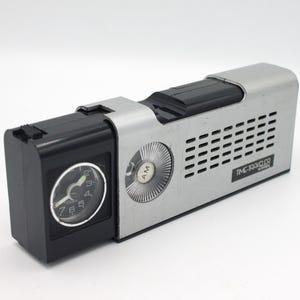 May include: A silver and black vintage AM radio with a clock on the side. The radio has a speaker grille and the text "TIME TRAVELLER" on the front.