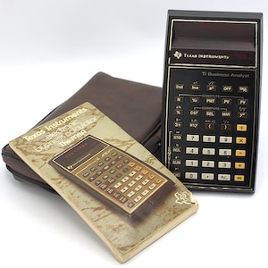 May include: A black Texas Instruments TI Business Analyst calculator with a brown top section. A brown leather case and a manual are next to the calculator. The manual reads "Texas Instruments electronic business calculator The MBA".