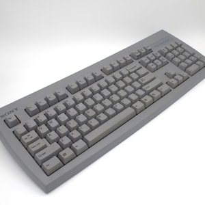 May include: A gray Sony computer keyboard with light gray keys. The keyboard has a standard QWERTY layout with function keys and a numeric keypad. The Sony logo is visible in the upper left corner. The keyboard is on a white background.