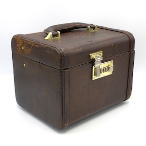 May include: A vintage brown suitcase with a handle and gold-colored hardware. The suitcase has a combination lock and shows signs of wear, suggesting it's been well-traveled. The boxy shape and sturdy construction indicate it's designed for carrying items.