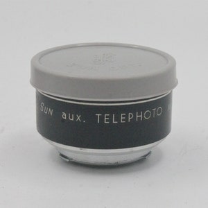May include: A black and silver telephoto lens attachment for a camera. The lens has a gray plastic cap with the text "Sun aux. Telephoto" printed on the side.
