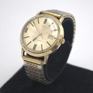 May include: A gold-toned Timex watch with a white face and black hands. The watch has a date window at the 3 o'clock position and says "Timex" and "Lefwind" on the face.