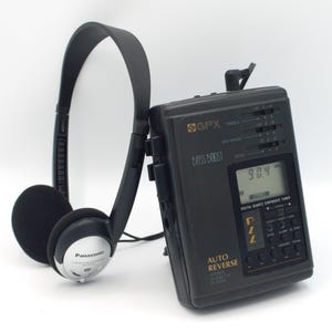 May include: A black and silver cassette player with a digital display and a built-in radio tuner. The player has a bass boost feature and an auto reverse function. It is paired with black headphones.