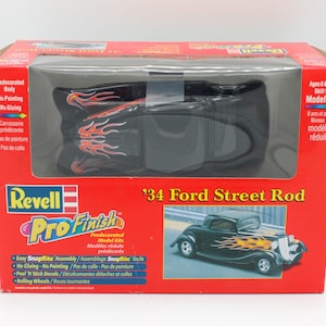 May include: A Revell Pro Finish model kit of a '34 Ford Street Rod. The model is black with red and yellow flames. The box features a photo of the assembled model and instructions for assembly.
