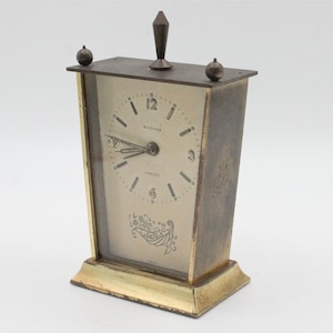 May include: A vintage brass alarm clock with a white face and black hands. The clock face says "Waltham" and "Jewelled".
