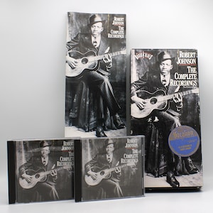 May include: A collection of Robert Johnson's "The Complete Recordings" on CD and album format. The album art features a black and white image of Robert Johnson playing a guitar. The album covers and CDs are in various sizes.