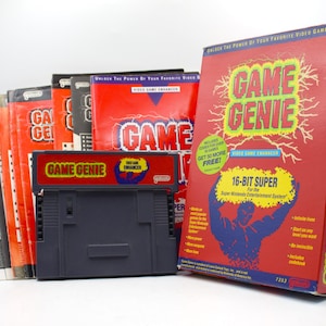 May include: A Game Genie video game enhancer cartridge for the Super Nintendo Entertainment System, accompanied by its original red and blue cardboard packaging box and several printed instruction manuals featuring the Game Genie logo and text.