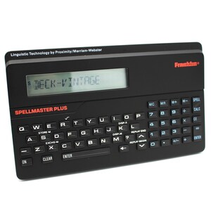 May include: A black Franklin Spellmaster Plus handheld spelling and calculator device with a blue LCD screen displaying "DECK-VINTAGE". The device has a QWERTY keyboard, a number pad, and various function buttons.