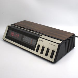 May include: Vintage Sears stereo alarm clock with a wood grain top and a digital red display showing 10:17. The clock has a silver face with black buttons and a radio tuner.