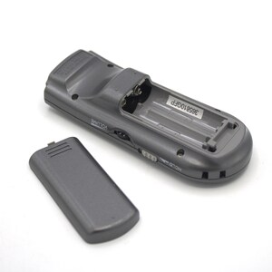 May include: A gray remote control with a battery compartment open, revealing two AA batteries. The remote has a volume knob, a hold button, and the text "3958106FP" printed on the inside of the battery compartment.