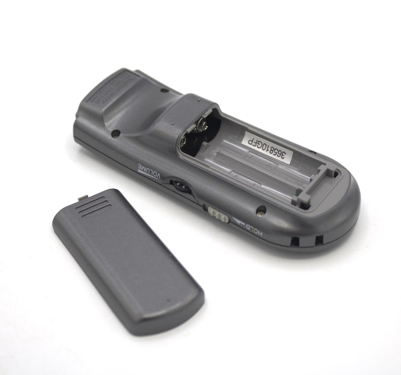 May include: A gray remote control with a battery compartment open, revealing two AA batteries. The remote has a volume knob, a hold button, and the text "3958106FP" printed on the inside of the battery compartment.