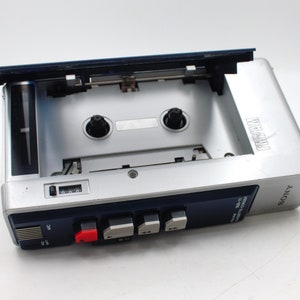 May include: Silver Sony WM-11 cassette player with the cassette door open. The player has a blue top and a red button. The word "FIVAN" is printed on the top of the player.