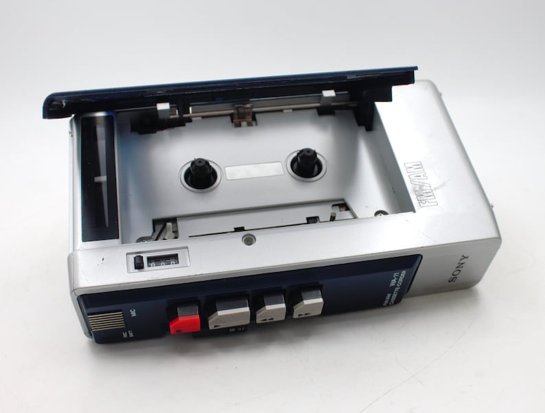 May include: Silver Sony WM-11 cassette player with the cassette door open. The player has a blue top and a red button. The word "FIVAN" is printed on the top of the player.