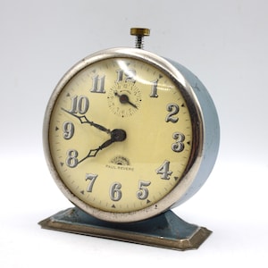 May include: A vintage blue alarm clock with a white face and black hands. The clock has a silver trim and the words "Paul Revere" on the face.