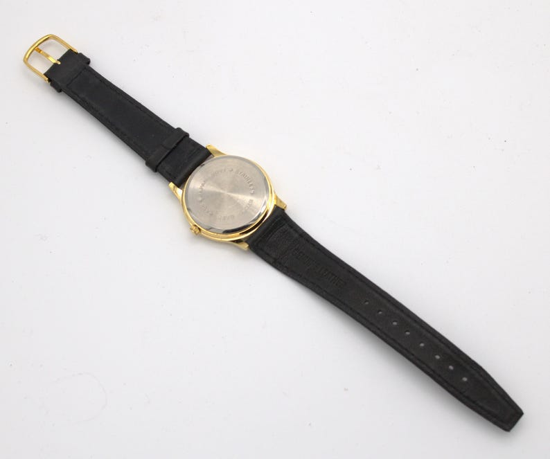 May include: A gold-toned wristwatch with a black leather band. The watch has a round face and a gold buckle. The back of the watch is silver-toned. The watch band is approximately 9 inches long.
