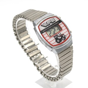 Peut inclure: Montre num&eacute;rique argent&eacute;e avec bracelet extensible. Le cadran de la montre a une bordure rouge et blanche avec le texte "WFE WHITE FARM EQUIPMENT" et un dessin de tracteur. L'&eacute;cran num&eacute;rique affiche l'heure.