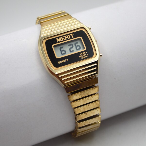 Vintage 1980s digital wristwatch LCD quartz display with light button polished gold tone finish elastic metal band black dial Merit 80s