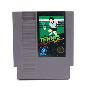 May include: A gray Nintendo Entertainment System cartridge for the game "Tennis." The label features a pixelated tennis player in blue and black, with the word "Tennis" in green and white. The Nintendo logo is visible.