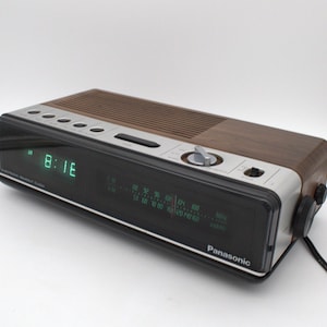 May include: A Panasonic electronic readout clock radio with a wood grain finish, a silver control panel, and a black front display. The digital clock shows 8:16 in green, and the analog radio tuner features AM and FM frequency scales.