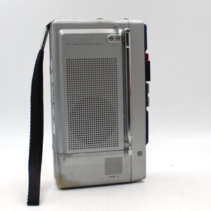 May include: A silver and gray Sony radio cassette recorder with a black carrying strap. The radio has a telescoping antenna and a speaker grill. The text "SONY" and "RADIO CASSETTE-CORDER" are visible on the front.