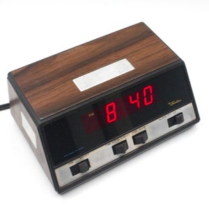 May include: A vintage wood-grain digital alarm clock with a red LED display showing the time 8:40 PM. The clock has several buttons for setting the alarm, time, and snooze.