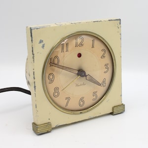 May include: A vintage white Westclox electric alarm clock with a round face and black hands. The clock has a red dot at the 12 o'clock position and gold accents around the face.