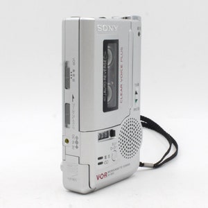 May include: A silver Sony microcassette recorder with a black strap. The recorder has a clear voice plus feature and an auto reverse function. The text "VOR" and "MICROCASSETTE CORD" are printed on the recorder.