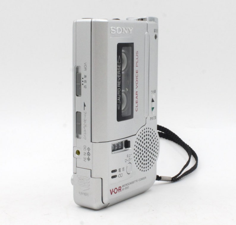 May include: A silver Sony microcassette recorder with a black strap. The recorder has a clear voice plus feature and an auto reverse function. The text "VOR" and "MICROCASSETTE CORD" are printed on the recorder.
