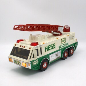 May include: A vintage Hess gasoline fire truck toy. The toy truck is white and green with a red extending ladder on top. The truck has the Hess logo and the word "Gasoline" printed on the side. The truck has red lights and black tires.