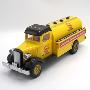 May include: A yellow Shell Oil Company tanker truck toy with black accents. The truck features the Shell logo and the text "Lubricants, Gasolines and Motor Oils." The front of the truck has the text "Shell 1935."