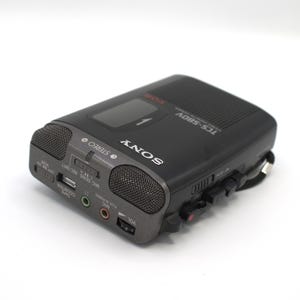 May include: A black Sony TCS-580V voice recorder with a dark gray front panel. The recorder has two built-in microphones, a volume control, and various input/output jacks. The word "SONY" is printed in white on the front.