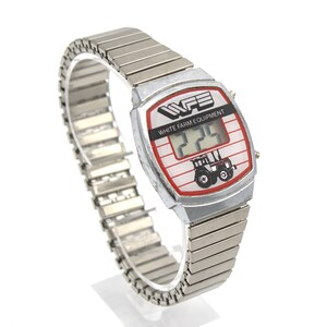 Peut inclure: Montre num&eacute;rique argent&eacute;e avec un cadran blanc et rouge. Le cadran affiche le texte "WHITE FARM EQUIPMENT" et un dessin de tracteur. La montre a un bracelet extensible argent&eacute;.