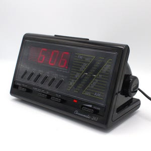May include: Black digital alarm clock displaying 6:06 in red. The clock has FM/AM radio functionality and a volume control. The brand name "Chronomatic-263" is printed on the front.