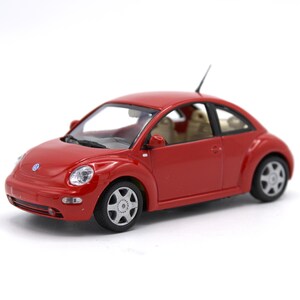 May include: A red toy car, a Volkswagen Beetle, is shown from a side angle. The car has a rounded shape, with a black antenna and silver wheels. The car's headlights and front bumper are visible.
