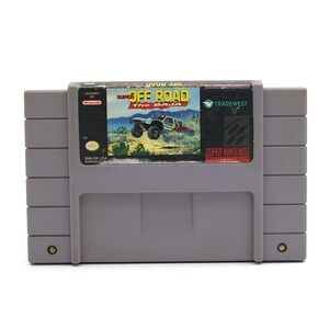 May include: A gray Super Nintendo game cartridge featuring the game "Super Off Road The Baja." The label shows a desert scene with a racing truck. The cartridge has the Nintendo and Tradewest logos.