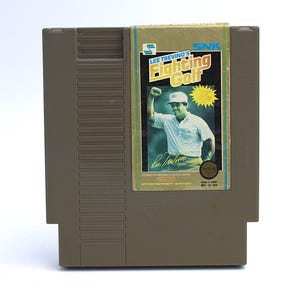 May include: A brown Nintendo Entertainment System (NES) game cartridge for "Lee Trevino's Fighting Golf." The label features a photo of Lee Trevino, the game's title, and the SNK logo. The cartridge is made in Japan.