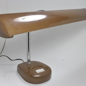 May include: A vintage desk lamp with a brown, curved shade and a chrome-colored stem. The base is brown with a white on/off switch. A black power cord extends from the base.
