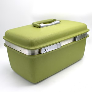 May include: A vintage olive green hard-sided travel case with a textured surface. The case has a silver-toned metal trim and handle, and a latch closure. The case is rectangular and has rounded corners.
